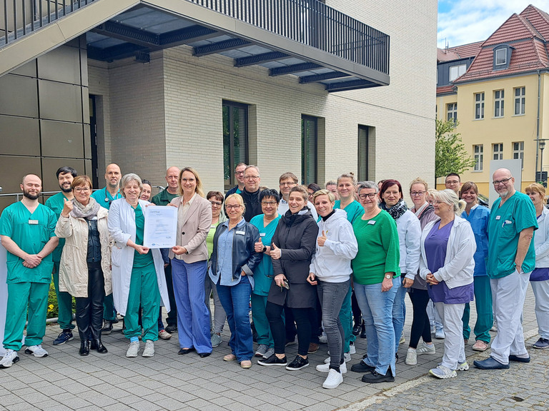 Mitarbeitende des Immanuel Klinikums Bernau vor dem Klinikgebäude mit dem Zertifikat Qualitätszertifikat DIN EN ISO 9001:2015 