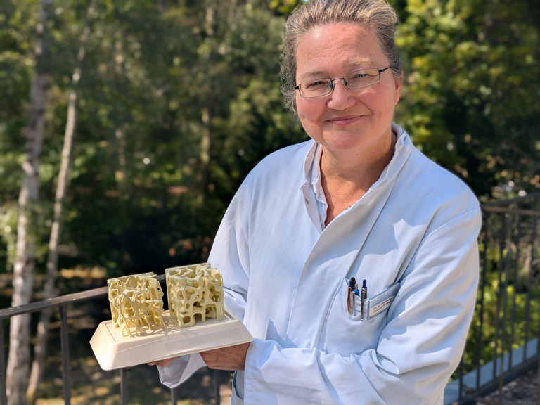 Dr. med. Katja Warnecke steht auf einem Balkon mit einem Modell in der Hand 