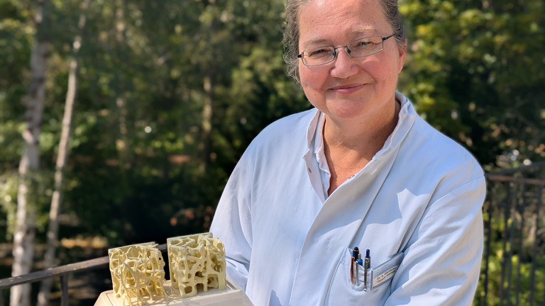 Dr. med. Katja Warnecke steht auf einem Balkon mit einem Modell in der Hand Dr. med. Katja Warnecke steht auf einem Balkon mit einem Modell in der Hand