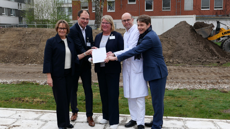 Hamburgs Sozialsenatorin Melanie Schlotzhauer, Amalie-Geschäftsführer Andreas Schneider, Pflegedirektorin Maike Sellentin, der Ärztliche Direktor Prof. Dr. Ernst von Dobschütz und der Konzerngeschäftsführer der Immanuel Albertinen Diakonie Dr. Thorsten Minuth (von links) halten symbolisch den Fördermittelbescheid über 53 Millionen Euro für den Neubau am Evangelischen Amalie Sieveking Krankenhaus in Hamburg-Volksdorf in die Kamera.