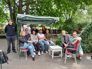 Eine Gruppe von Auszubildenden sitzt mit der Ausbildungskoordinatorin am Campus Wannsee, Jessica Paul, zusammen auf einer Minigolfanlage beim Azubi-Tag 2025 von Werkstück Raumgestaltung und Versorgungstechnik in Berlin