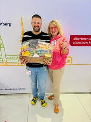 Übergabe des Präsentkorbs an den Gewinner des Pflegequiz am Messestand des Albertinen Krankenhauses