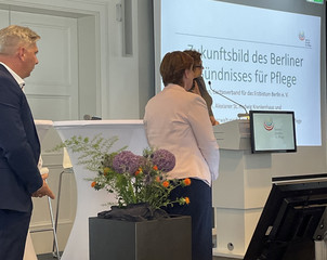 Martin Kringe steht neben dem Podium auf der Bühne und hört der Rede von Senatorin Ina Czyborra zu