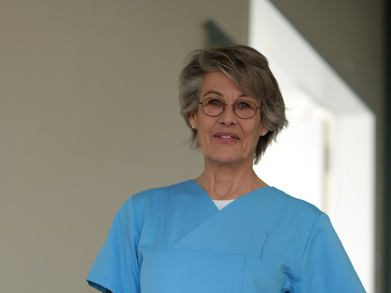 Stefanie Heldt, Leitung der Therapeutischen Dienste im Evangelischen Amalie Sieveking Krankenhaus, steht in blauer Arbeitskleidung in einem Klinikflur und blickt in die Kamera.