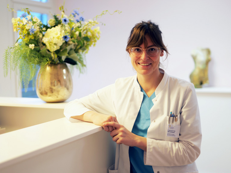 Dr. (univ. Pecs) Zsofia Danckwardt, Leitende Oberärztin Klinik für Gynäkologie und Geburtshilfe sowie Sektionsleiterin Urogynäkologie im Evangelischen Amalie Sieveking Krankenhaus in Hamburg, blickt angelehnt an einen Empfangstresen mit großem Blumenstrauß im Hintergrund in die Kamera