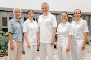 Ein Team des Interdisziplinären Therapiezentrums steht in weißer Funktionskleidung vor dem Zentrum für Altersmedizin des Albertinen Krankenhauses in Hamburg-Schnelsen und blickt in die Kamera