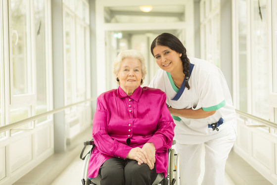 Eine Seniorin im Rollstuhl und eine Pflegefachkraft lächeln in die Kamera, Ausbildung Berufliche Pflegeausbildung BPA, Pflegefachmann, Pflegefachfrau, Gesundheits- und Pflegeassistenz, Residenz am Wiesenkamp, Feierabendhaus, Hamburg, Volksdorf Eine Seniorin im Rollstuhl und eine Pflegefachkraft lächeln in die Kamera