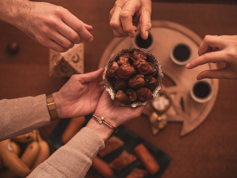 Gemeinsames Teilen von Datteln beim Zuckerfest (Eid al-Fitr) nach dem Ramadan – Hände greifen nach süßen Speisen als Zeichen von Gemeinschaft und Freude