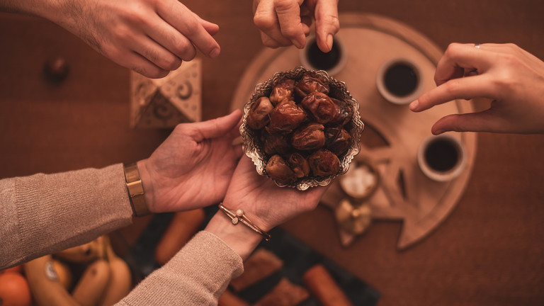 Gemeinsames Teilen von Datteln beim Zuckerfest (Eid al-Fitr) nach dem Ramadan – Hände greifen nach süßen Speisen als Zeichen von Gemeinschaft und Freude