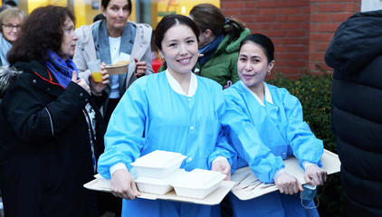 Zwei Pflegekräfte in blauer Funktionskleidung halten Tabletts mit verpacktem Essen und blicken in die Kamera bei der Weihnachtsfeier 2025 von Amalie Sieveking Krankenhaus, Residenz am Wiesenkamp, Feierabendhaus Volksdorf und Albertinen Kindertagesstätte Volksdorf auf dem Gesundheitscampus Volksdorf in Hamburg