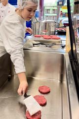 Schülerin brät beim Girls’ Day in der Zentralküche der Albertinen Services in Rellingen Burger-Patties auf einer Grillplatte.