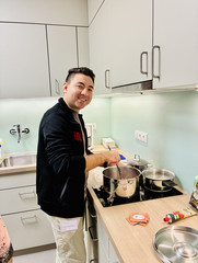 Beim gemeinsamen Kochen in der Küche rührt eine der Pflegekräfte gut gelaunt in einem Topf und bereitet ein Gericht zu.