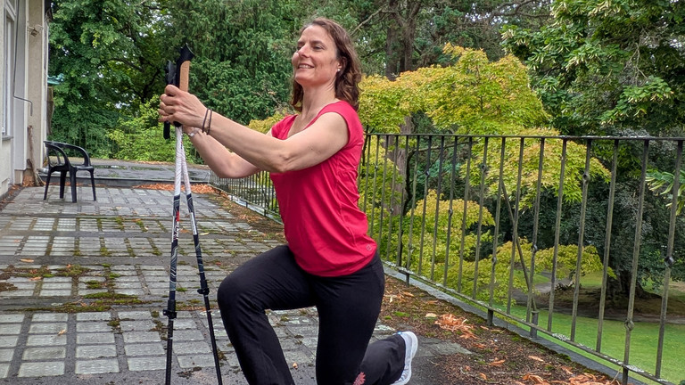 Therapeutin führt Übung mithilfe von Nordic Walking Stöcken aus Therapeutin führt Übung mithilfe von Nordic Walking Stöcken aus