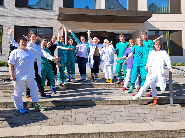 Mitarbeitende des Immanuel Klinikum Bernau stehen vor dem Eingang und zeigen ihre bunten Socken anlässlich des Welt-Down-Syndrom Tages