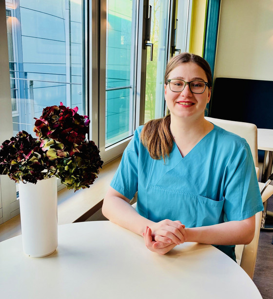 Pflegekraft in blauer Dienstkleidung sitzt lächelnd an einem hellen Tisch im Albertinen Krankenhaus. Modernes Umfeld, offene und freundliche Atmosphäre, die internationale Fachkräfte und eine erfolgreiche berufliche Integration im Pflegebereich widerspiegelt. Pflegekraft in blauer Dienstkleidung sitzt lächelnd an einem hellen Tisch im Albertinen Krankenhaus. Modernes Umfeld, offene und freundliche Atmosphäre, die internationale Fachkräfte und eine erfolgreiche berufliche Integration im Pflegebereich widerspiegelt.