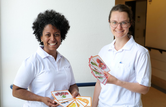 Zwei neorologische Therapeutinnen stehen in weißer Funktionskleidung mit Memorycards in den Händen auf einem Krankenhausflur und lächeln in die Kamera im Interdisziplinären Therapiezentrum im Albertinen Krankenhaus Hamburg Zwei neorologische Therapeutinnen stehen in weißer Funktionskleidung mit Memorycards in den Händen auf einem Krankenhausflur und lächeln in die Kamera im Interdisziplinären Therapiezentrum im Albertinen Krankenhaus Hamburg