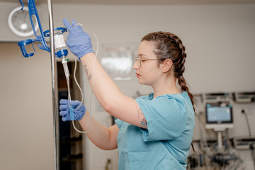 Eine jüngere Krankenpflegerin in grünblauer Funktionskleidung steht an einem Infusionsständer und bereitet eine Infusion vor in einem Patientenzimmer im Albertinen Krankenhaus in Hamburg-Schnelsen 