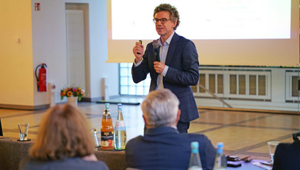 Ein Redner spricht bei seinem Vortrag mit einem Mikrofon in der Hand vor dem Publikum beim Einführungssymposium „Die Zukunft ist alt!“ von Priv.-Doz. Dr. Gödel, Chefarzt der Klinik für Geriatrie im Albertinen Zentrum für Altersmedizin im Albertinen Krankenhaus in Hamburg.