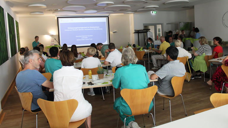 Teilnehmende Hausärztinnen und Hausärzte sitzen an Tischen und hören einem Vortrag mit Präsentation auf einer Leinwand zu - Immanuel Klinikum Bernau - Nachricht Teilnehmende Hausärztinnen und Hausärzte sitzen an Tischen und hören einem Vortrag mit Präsentation auf einer Leinwand zu - Immanuel Klinikum Bernau - Nachricht