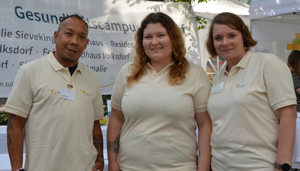 Drei Pflegekräfte des Feierabendhauses Volksdorf und der Residenz am Wiesenkamp blicken in die Kamera an den Ständen des Gesundheitscampus Volksdorf der Immanuel Albertinen Diakonie beim Stadtteilfest Volksdorf in Hamburg