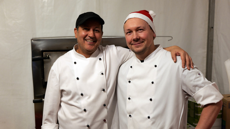 Zwei Köche der Albertinen Services Hamburg in weißen Kochschürzen blicken fröhlich in die Kamera bei der Weihnachtsfeier 2025 von Amalie Sieveking Krankenhaus, Residenz am Wiesenkamp, Feierabendhaus Volksdorf und Albertinen Kindertagesstätte Volksdorf auf dem Gesundheitscampus Volksdorf in Hamburg