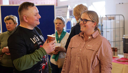 Ein Mitarbeiter mit einem Becher in der Hand unterhält sich fröhlich mit einer Kollegin bei der Weihnachtsfeier 2025 von Amalie Sieveking Krankenhaus, Residenz am Wiesenkamp, Feierabendhaus Volksdorf und Albertinen Kindertagesstätte Volksdorf auf dem Gesundheitscampus Volksdorf in Hamburg
