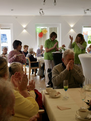 Zwei Pflegekräfte in grüner Arbeitskleidung singen und klatschen im voll besetzten und bunt geschmückten Saal bei der Wiedereröffnung der Tagespflegestätte für ältere Menschen im Immanuel Seniorenzentrum Kläre Weist in Petershagen Zwei Pflegekräfte in grüner Arbeitskleidung singen und klatschen im voll besetzten und bunt geschmückten Saal bei der Wiedereröffnung der Tagespflegestätte für ältere Menschen im Immanuel Seniorenzentrum Kläre Weist in Petershagen