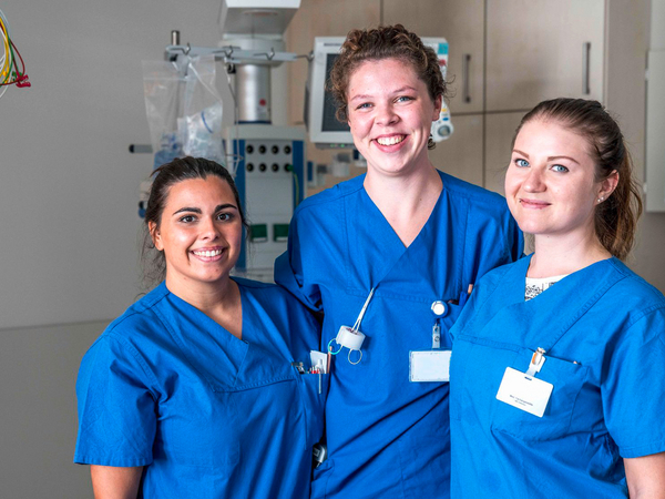 Drei junge Pflegefachkräfte in Arbeitskleidung freuen sich über neue Kolleginnen und Kollegen