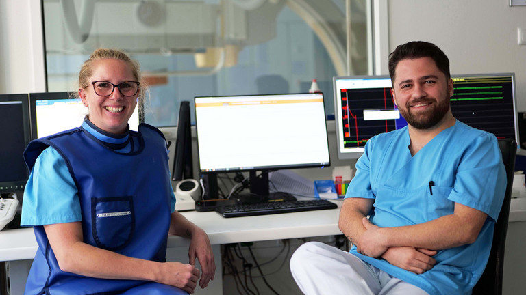 Zwei Pflegefachkräfte der kardiologischen Funktionsdiagnostik vor Monitoren lächeln in die Kamera im Albertinen Krankenhaus in Hamburg-Schnelsen