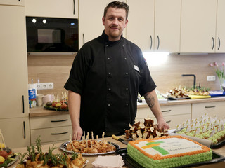 Ein Koch in schwarzer Arbeitskleidung steht hinter dem Kuchen- und Fingerfoodbüffet und blickt in die Kamera bei der Wiedereröffnung der Tagespflegestätte für ältere Menschen im Immanuel Seniorenzentrum Kläre Weist in Petershagen Ein Koch in schwarzer Arbeitskleidung steht hinter dem Kuchen- und Fingerfoodbüffet und blickt in die Kamera bei der Wiedereröffnung der Tagespflegestätte für ältere Menschen im Immanuel Seniorenzentrum Kläre Weist in Petershagen