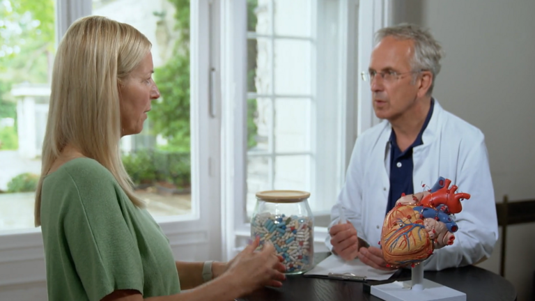 Prof. Dr. Michalsen und eine Patientin stehen an einem Tisch mit einem Herzmodell und unterhalten sich