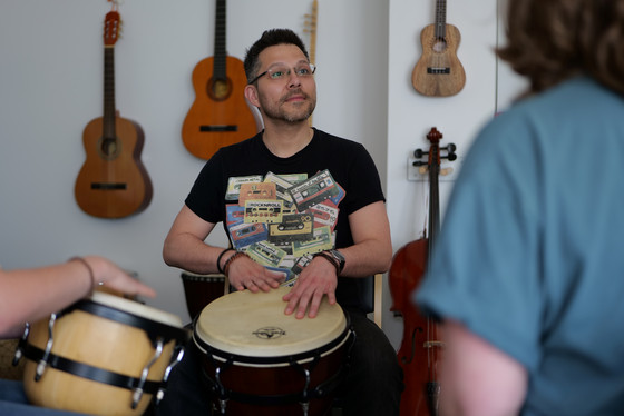 Ein Musiktherapeut sitzt an einer Trommel in einem Raum mit mehreren Therapieteilnehmenden und Instrumenten an der Wand im Interdisziplinären Therapiezentrum im Albertinen Krankenhaus Hamburg Ein Musiktherapeut sitzt an einer Trommel in einem Raum mit mehreren Therapieteilnehmenden und Instrumenten an der Wand im Interdisziplinären Therapiezentrum im Albertinen Krankenhaus Hamburg