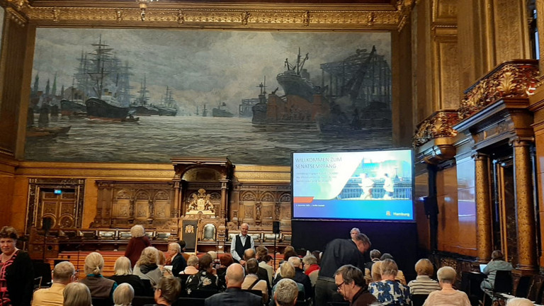 Blick über die Stuhlreihen mit Publikum im Festsaal des Hamburger Rathauses Richtung Podium mit einem großen Monitor zum Senatsempfang für ehrenamtlich engagierte Menschen mit Ehrung der Ehrenamtlichen im Albertinen Haus Hamburg Blick über die Stuhlreihen mit Publikum im Festsaal des Hamburger Rathauses Richtung Podium mit einem großen Monitor zum Senatsempfang für ehrenamtlich engagierte Menschen mit Ehrung der Ehrenamtlichen im Albertinen Haus Hamburg