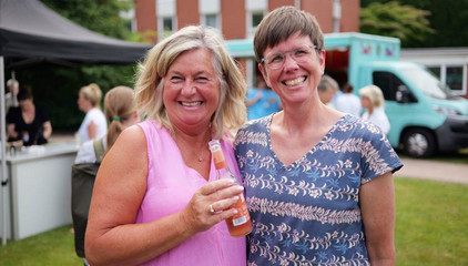 Zwei Mitarbeiterinnen stehen nebeneinander und strahlen in die Kamera beim Sommerfest 2026 auf dem Gesundheitscampus Volksdorf des Evangelischen Amalie Sieveking Krankenhauses, der Residenz am Wiesenkamp, des Feierabendhauses Volksdorf und der Albertinen Kindertagesstätte Volksdorf. 