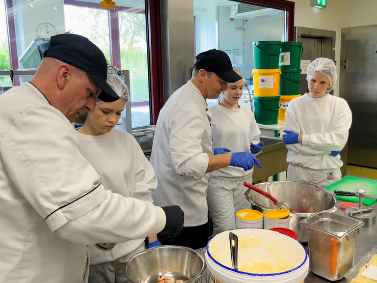Mitarbeiter der Zentralküche zeigen Schülerinnen beim Girls’ Day praktische Arbeitsschritte bei der Zubereitung von Speisen.