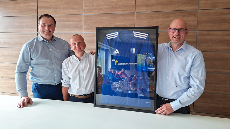 Vorstnadsmitglied des FC Strausber, Daniel Thamm und Frank Volkmer halten einen Bilderrahmen mit einem Trikot des FC Strausberg