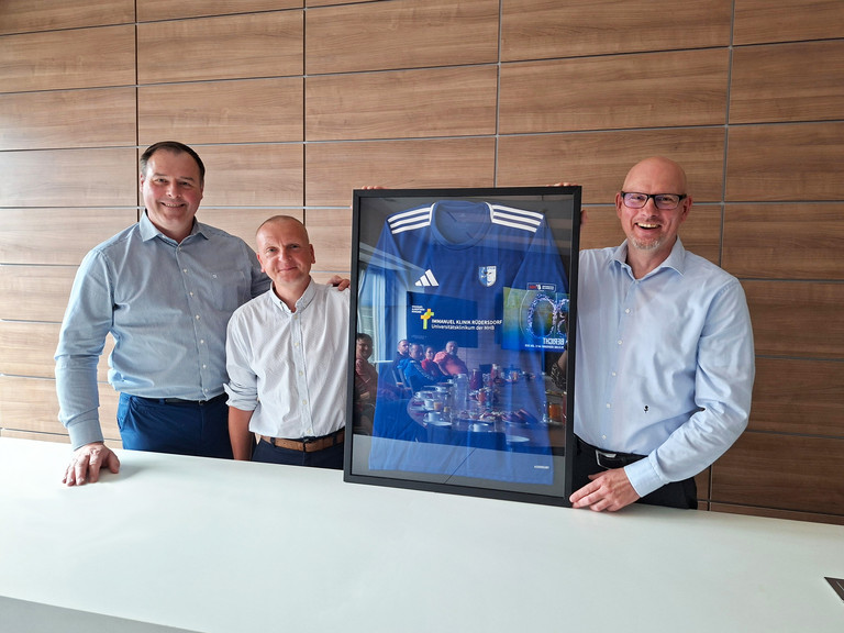 Vorstnadsmitglied des FC Strausber, Daniel Thamm und Frank Volkmer halten einen Bilderrahmen mit einem Trikot des FC Strausberg
