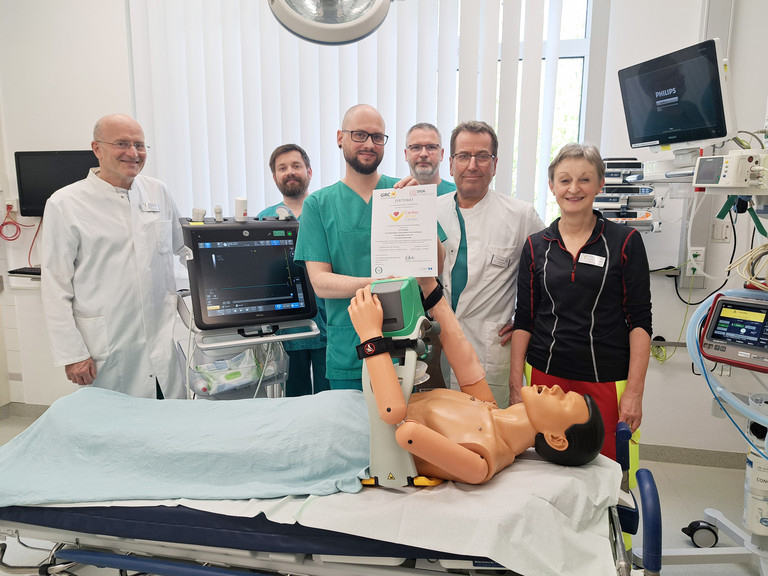 Im Schockraum der Zentralen Notaufnahme im Immanuel Klinikum Bernau Herzzentrum Brandenburg zeigen die Spezialistinnen und Spezialisten aus der Zentralen Notaufnahme, der Intensivmedizin und der Kardiologie des Immanuel Klinikum Bernau Herzzentrum Brandenburg stolz das Zertifikat „Cardiac Arrest Center“