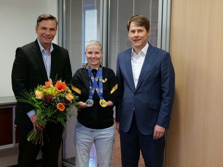 Stephanie Grebe zeigt ihre Gold- und Silbermedaille der Para-Tischtennis-Europameisterschaft und wird von Andreas Mende und Dr. Thorsten Minuth herzlich in der Immanuel Albertinen Diakonie beglückwünscht.