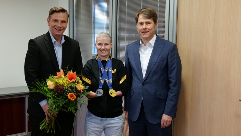 Stephanie Grebe zeigt ihre Gold- und Silbermedaille der Para-Tischtennis-Europameisterschaft und wird von Andreas Mende und Dr. Thorsten Minuth herzlich in der Immanuel Albertinen Diakonie beglückwünscht.