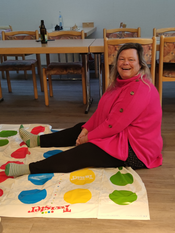 Eine Mitarbeiterin sitzt lachend auf einer Spieldecke in der Immanuel Begegnungsstätte Ecktannen im Heilbad Waren beim gemeinsamen Spieleabend für Mitarbeitende der Seniorenpflegeeinrichtung mit Tagespflegeangebot Immanuel Haus Ecktannen.