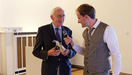 Prof. Wolfgang von Renteln-Kruse überreicht dem Gastgeber ein Präsent und spricht in ein Mikrofon beim Einführungssymposium „Die Zukunft ist alt!“ von Priv.-Doz. Dr. Gödel, Chefarzt der Klinik für Geriatrie im Albertinen Zentrum für Altersmedizin im Albertinen Krankenhaus in Hamburg.