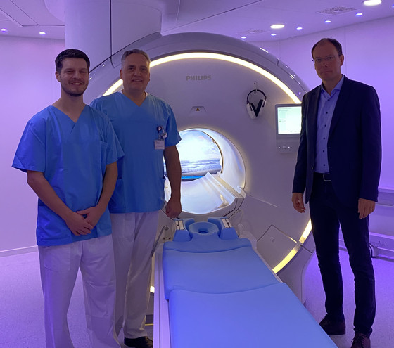 Richard Grundherr, Prof. Christoph Weber und Andreas Schneider stehen in einem dunkellila illuminierten Raum vor dem neuen MRT-System im Immanuel Albertinen Zentrum für Radiologie am Standort Ev. Amalie Sieveking Krankenhaus in Hamburg und blicken in die Kamera Richard Grundherr, Prof. Christoph Weber und Andreas Schneider stehen in einem dunkellila illuminierten Raum vor dem neuen MRT-System im Immanuel Albertinen Zentrum für Radiologie am Standort Ev. Amalie Sieveking Krankenhaus in Hamburg und blicken in die Kamera