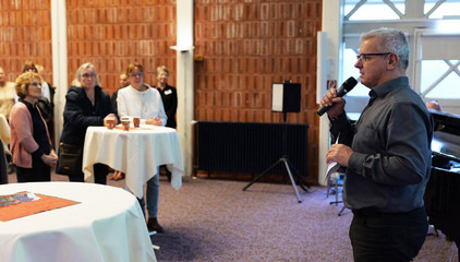 Pastor und Klinikseelsorger Roger Bahr spricht mit einem Mikrofon in der Hand zu den Gästen bei der Weihnachtsfeier 2025 von Amalie Sieveking Krankenhaus, Residenz am Wiesenkamp, Feierabendhaus Volksdorf und Albertinen Kindertagesstätte Volksdorf auf dem Gesundheitscampus Volksdorf in Hamburg