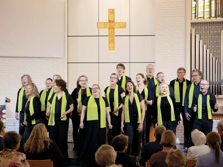 Die Mitglieder des Albertinen-Mitarbeitenden-Gospelchors singen bei einem Gospelkonzert auf der Bühne der Kiche beim Albertinen Krankenhaus in festlicher schwarzer Kleidung mit grünen Schals.
