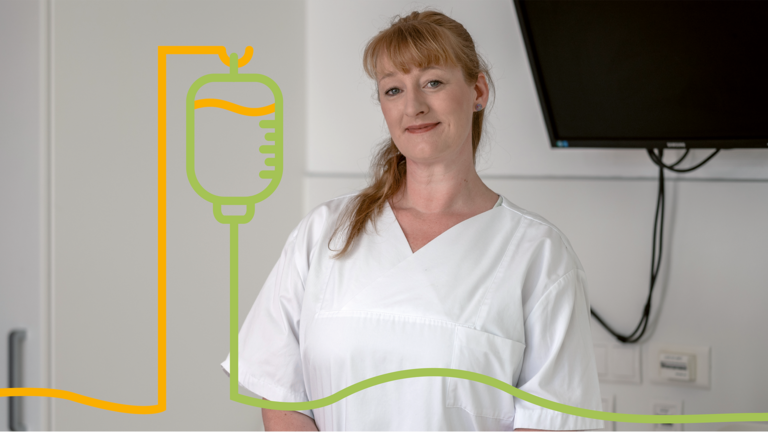 Pflegefachkraft steht in einem Patientenzimmer und lächelt in die Kamera. Das Bild steht für professionelle Pflege, Einfühlungsvermögen und die Betreuung von Patientinnen und Patienten.
