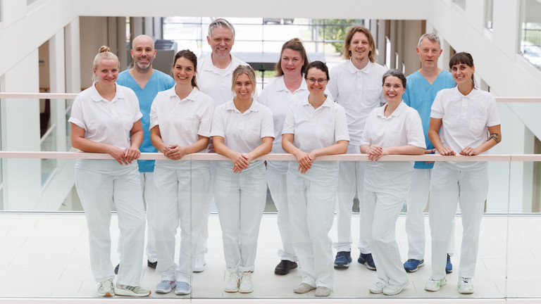 Das Team der Neurologie des Interdisziplinären Therapiezentrums im Albertinenkrankenhaus steht in Dienstkleidung freundlich in die Kamera blickend auf dem Flur Das Team der Neurologie des Interdisziplinären Therapiezentrums im Albertinenkrankenhaus steht in Dienstkleidung freundlich in die Kamera blickend auf dem Flur