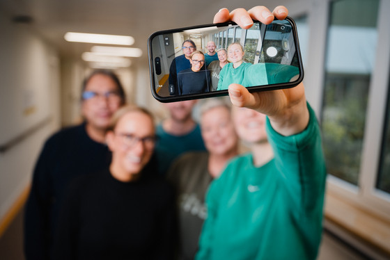 Eine Pflegefachkraft macht ein Selfie ihres lächelnden Teams auf dem Stationsflur der Klinik für Psychiatrie und Psychotherapie im Albertinen Krankenhaus in Hamburg und hält das Smartphone mit dem sichtbaren Bildschirm nach oben. Eine Pflegefachkraft macht ein Selfie ihres lächelnden Teams auf dem Stationsflur der Klinik für Psychiatrie und Psychotherapie im Albertinen Krankenhaus in Hamburg und hält das Smartphone mit dem sichtbaren Bildschirm nach oben.
