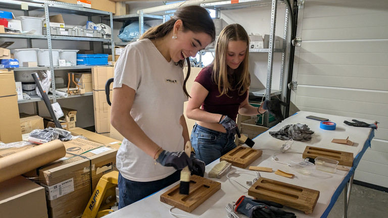 Mädchen haben Spaß beim Auftragen von Holzöl auf Handyhalter - Werkstück Raumgestaltung & Versorgungstechnik