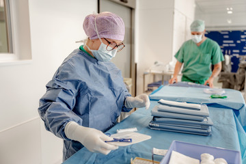 Zwei OP-Fachkräfte mit Kopfhauben und Funktionskleidung stehen an einem steril abgedeckten Tisch im Vorbereitungsbereich des Zentral-OP und bereiten verpackte Materialien für eine Operation vor im Albertinen Krankenhaus in Hamburg